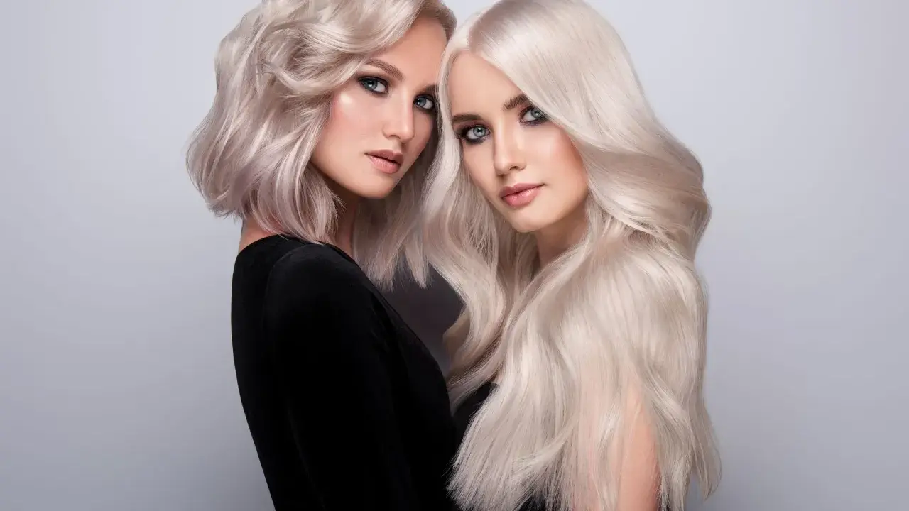Dwie kobiety z olśniewającymi, **zimnymi blond włosami**. Jedna ma krótką, falowaną fryzurę, druga długie, proste pasma.