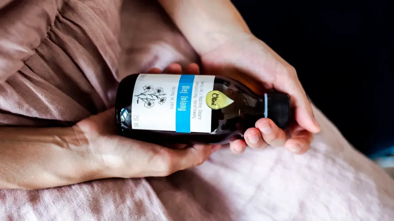 Dłonie trzymają butelkę oleju lnianego. To naturalny produkt, który ma szerokie olej lniany zastosowanie w kuchni i kosmetyce.