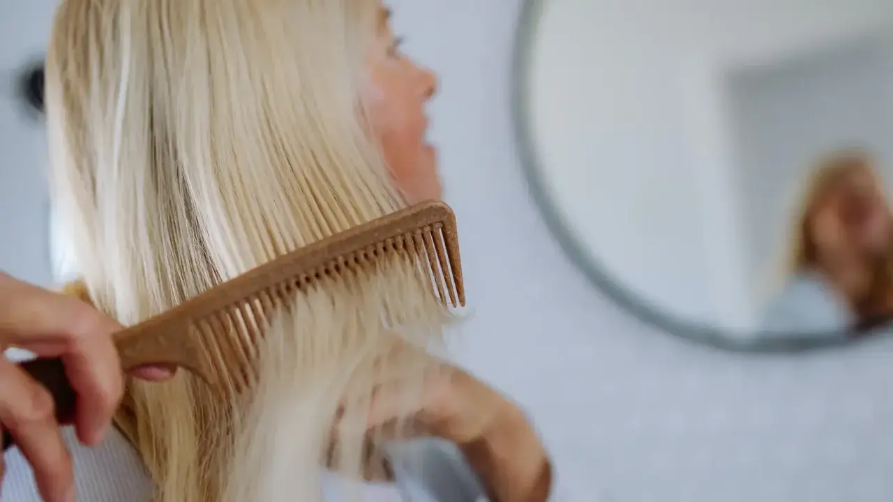 Kobieta czesze blond włosy, szukając rozwiązań co na wypadanie włosów po ciąży.