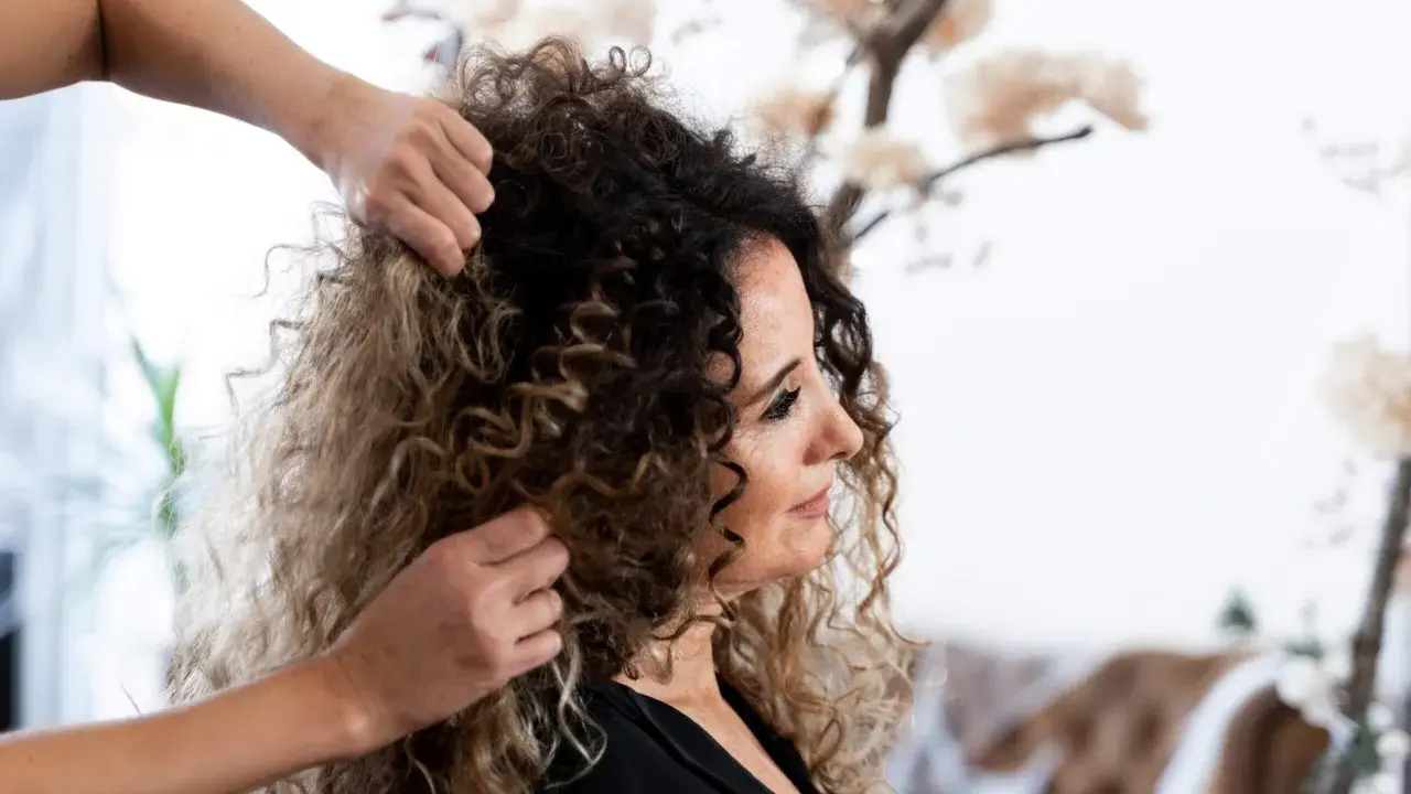 Stylista układa kręcone włosy klientki, przygotowując się do strzyżenia. Wskazówki, jak obciąć kręcone włosy, pomogą uzyskać idealną fryzurę.
