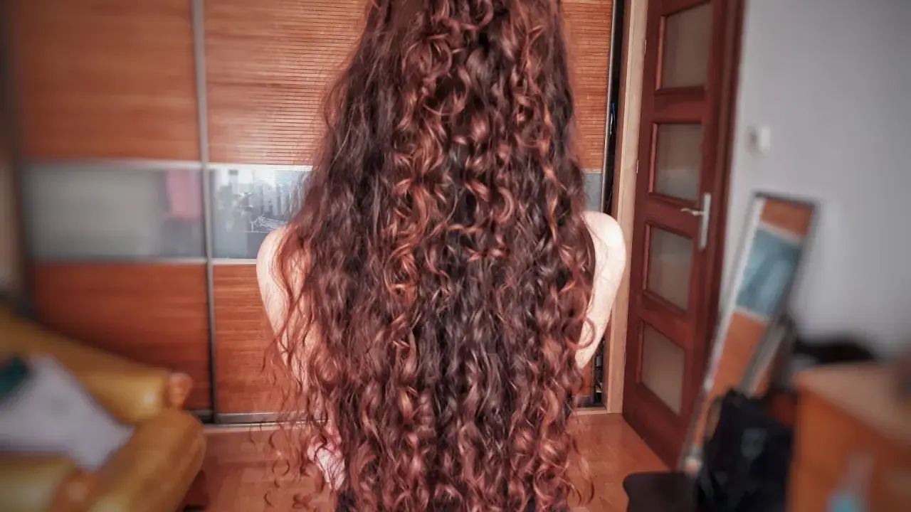 Długie, falowane włosy w odcieniu rudego brązu, ułożone w luźny kok. Efekt pięknej, naturalnej wavy hair routine.