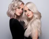 Dwie kobiety z olśniewającymi, **zimnymi blond włosami**. Jedna ma krótką, falowaną fryzurę, druga długie, proste pasma.