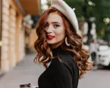 Rudowłosa kobieta w beretce i czarnym golfie, z burzą falowanych włosów. Poznaj sekrety, jak dbać o falowane włosy, by wyglądały tak zjawiskowo!