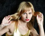 Blondynka w złotym topie, z grzywką, która odrasta, bawi się włosami na tle czarnego futra.