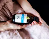 Dłonie trzymają butelkę oleju lnianego. To naturalny produkt, który ma szerokie olej lniany zastosowanie w kuchni i kosmetyce.