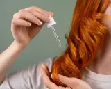 Dłoń z pipetką z olejkiem zbliża się do rudych włosów. Zastanawiasz się, jak długo trzymać olej na włosach dla najlepszych efektów?