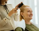 Fryzjer do kręconych włosów czesze blondynkę. Kobieta uśmiecha się, czując się komfortowo.