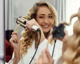 Uśmiechnięta blondynka tworzy połamane fale na krótkich włosach za pomocą lokówki.
