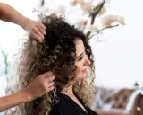 Stylista układa kręcone włosy klientki, przygotowując się do strzyżenia. Wskazówki, jak obciąć kręcone włosy, pomogą uzyskać idealną fryzurę.