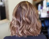 Kobieta z falowanymi włosami w odcieniach brązu i subtelnymi blond pasemkami.