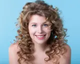 Uśmiechnięta blondynka z bujnymi lokami, efekt idealnego strzyżenia włosów kręconych.