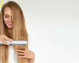 Uśmiechnięta blondynka pokazuje, jak używać prostownicy do włosów, tworząc idealnie gładką fryzurę.