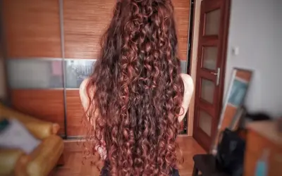 Długie, falowane włosy w odcieniu rudego brązu, ułożone w luźny kok. Efekt pięknej, naturalnej wavy hair routine.
