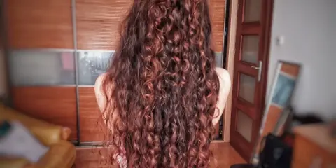 Długie, falowane włosy w odcieniu rudego brązu, ułożone w luźny kok. Efekt pięknej, naturalnej wavy hair routine.