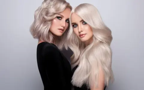 Dwie kobiety z olśniewającymi, **zimnymi blond włosami**. Jedna ma krótką, falowaną fryzurę, druga długie, proste pasma.