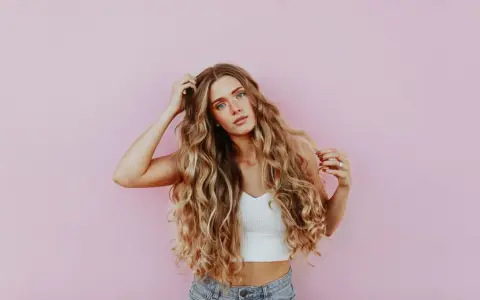Kobieta z falowanymi blond włosami, które wyglądają na zdrowe i lśniące, jakby użyto krzemu na włosy.