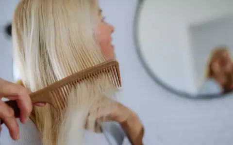 Kobieta czesze blond włosy, szukając rozwiązań co na wypadanie włosów po ciąży.