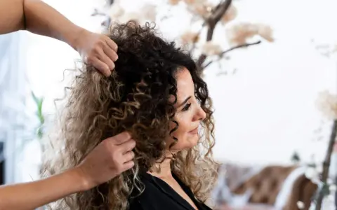Stylista układa kręcone włosy klientki, przygotowując się do strzyżenia. Wskazówki, jak obciąć kręcone włosy, pomogą uzyskać idealną fryzurę.