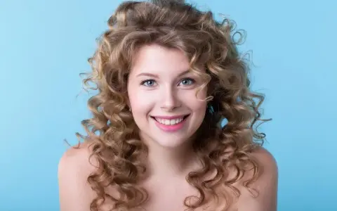 Uśmiechnięta blondynka z bujnymi lokami, efekt idealnego strzyżenia włosów kręconych.