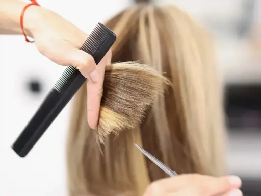 Fryzjerka tworzy modną fryzurę na szwedkę, precyzyjnie modelując blond włosy nożyczkami i grzebieniem.