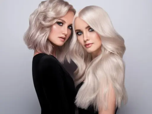 Dwie kobiety z olśniewającymi, **zimnymi blond włosami**. Jedna ma krótką, falowaną fryzurę, druga długie, proste pasma.