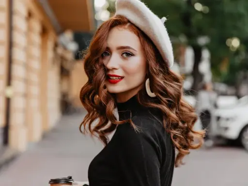 Rudowłosa kobieta w beretce i czarnym golfie, z burzą falowanych włosów. Poznaj sekrety, jak dbać o falowane włosy, by wyglądały tak zjawiskowo!