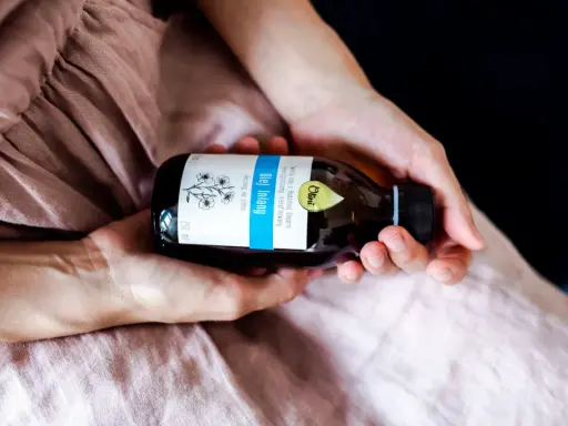 Dłonie trzymają butelkę oleju lnianego. To naturalny produkt, który ma szerokie olej lniany zastosowanie w kuchni i kosmetyce.