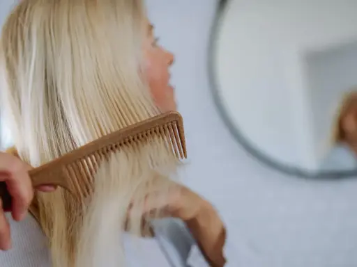 Kobieta czesze blond włosy, szukając rozwiązań co na wypadanie włosów po ciąży.