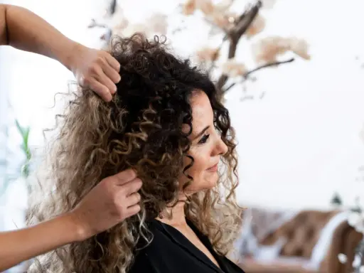 Stylista układa kręcone włosy klientki, przygotowując się do strzyżenia. Wskazówki, jak obciąć kręcone włosy, pomogą uzyskać idealną fryzurę.