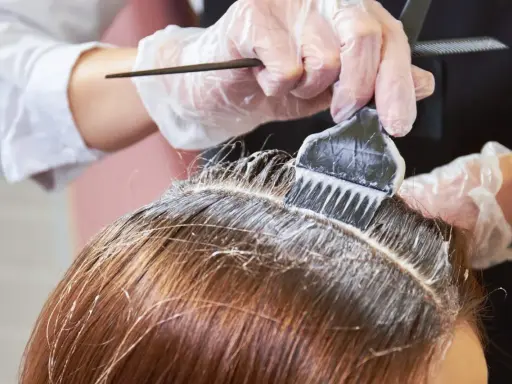 Profesjonalne farbowanie odrostów. Rękawiczki i pędzel z farbą precyzyjnie aplikują produkt na linię włosów.