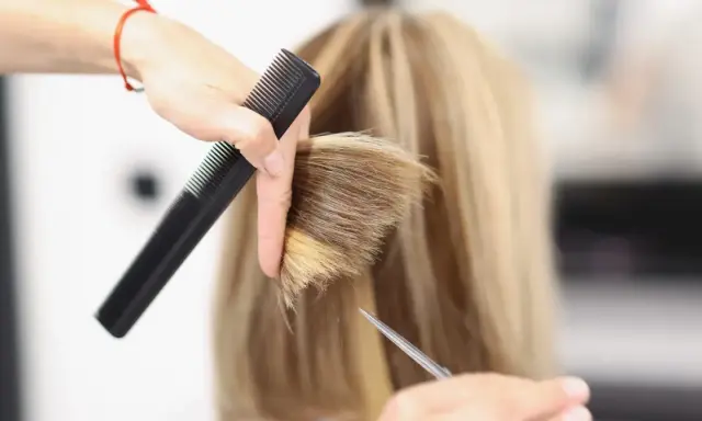 Fryzjerka tworzy modną fryzurę na szwedkę, precyzyjnie modelując blond włosy nożyczkami i grzebieniem.