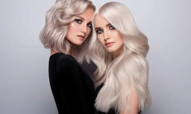 Dwie kobiety z olśniewającymi, **zimnymi blond włosami**. Jedna ma krótką, falowaną fryzurę, druga długie, proste pasma.