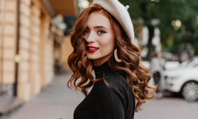 Rudowłosa kobieta w beretce i czarnym golfie, z burzą falowanych włosów. Poznaj sekrety, jak dbać o falowane włosy, by wyglądały tak zjawiskowo!