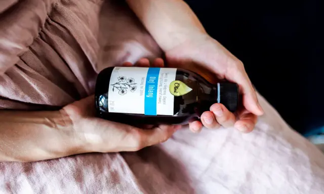 Dłonie trzymają butelkę oleju lnianego. To naturalny produkt, który ma szerokie olej lniany zastosowanie w kuchni i kosmetyce.
