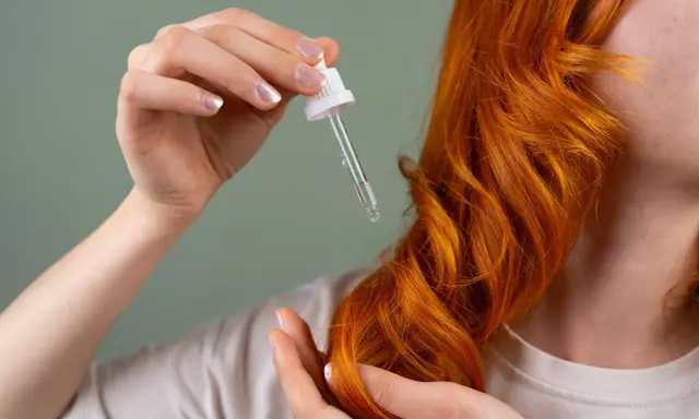 Dłoń z pipetką z olejkiem zbliża się do rudych włosów. Zastanawiasz się, jak długo trzymać olej na włosach dla najlepszych efektów?