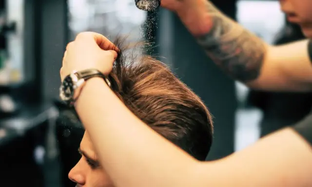 Stylista pokazuje, jak używać pudru do włosów, aplikując go na męską fryzurę dla objętości i tekstury.