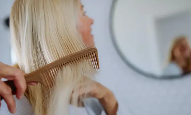 Kobieta czesze blond włosy, szukając rozwiązań co na wypadanie włosów po ciąży.