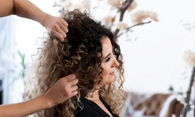 Stylista układa kręcone włosy klientki, przygotowując się do strzyżenia. Wskazówki, jak obciąć kręcone włosy, pomogą uzyskać idealną fryzurę.