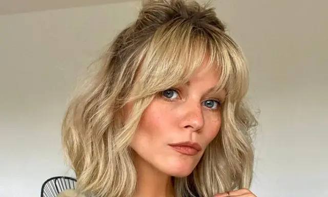 Kobieta z niebieskimi oczami i piegami, z falowanymi blond włosami i cieniowaną grzywką, upiętymi w luźny kok.