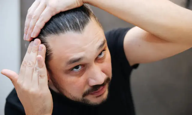 Mężczyzna sprawdza swoje włosy, martwiąc się o kreatynę a wypadanie włosów.