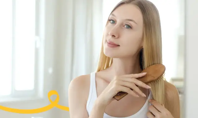 Kobieta szczotkuje włosy, przygotowując je na domowy peeling do skóry głowy.