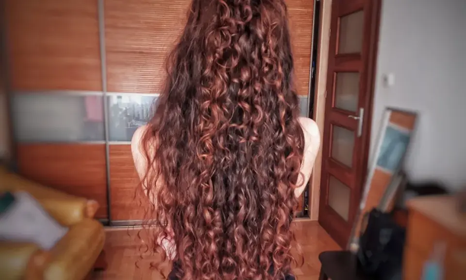 Długie, falowane włosy w odcieniu rudego brązu, ułożone w luźny kok. Efekt pięknej, naturalnej wavy hair routine.