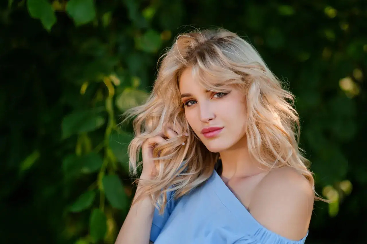 Blondynka w błękitnej bluzce, z lekko przetłuszczonymi włosami, dotyka ich dłonią.