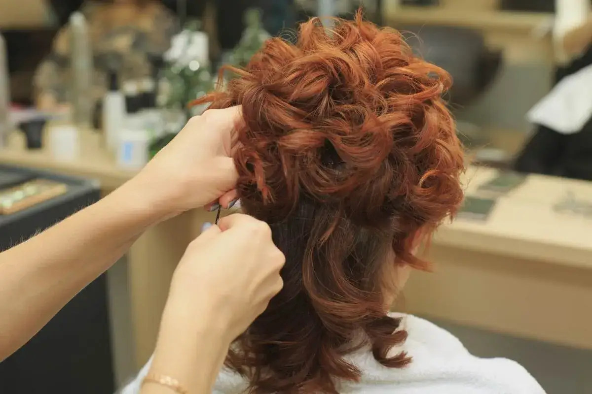 Fryzjer do kręconych włosów dopina kosmyki, tworząc elegancką fryzurę.