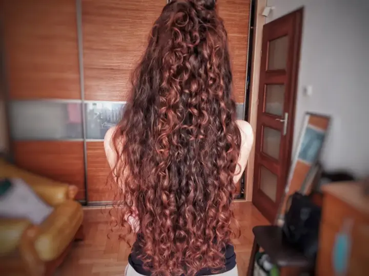 Długie, falowane włosy w odcieniu rudego brązu, ułożone w luźny kok. Efekt pięknej, naturalnej wavy hair routine.